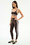 A woman wears the SPLITS59 Bianca High Waist Rigor 7/8 leggings in Dark Chocolate/White, featuring white side stripes and performance fabric, paired with a matching sports bra and black-and-white sneakers.