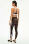 A woman stands in a studio, facing away, wearing SPLITS59's Bianca High Waist Rigor 7/8 leggings in Dark Chocolate/White with a matching sports bra and brown sneakers, all crafted from performance fabric.