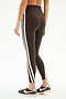 Someone wearing SPLITS59's Bianca High Waist Rigor 7/8 leggings in Dark Chocolate/White, featuring two white side stripes, and black Nike sneakers stands against a plain background.