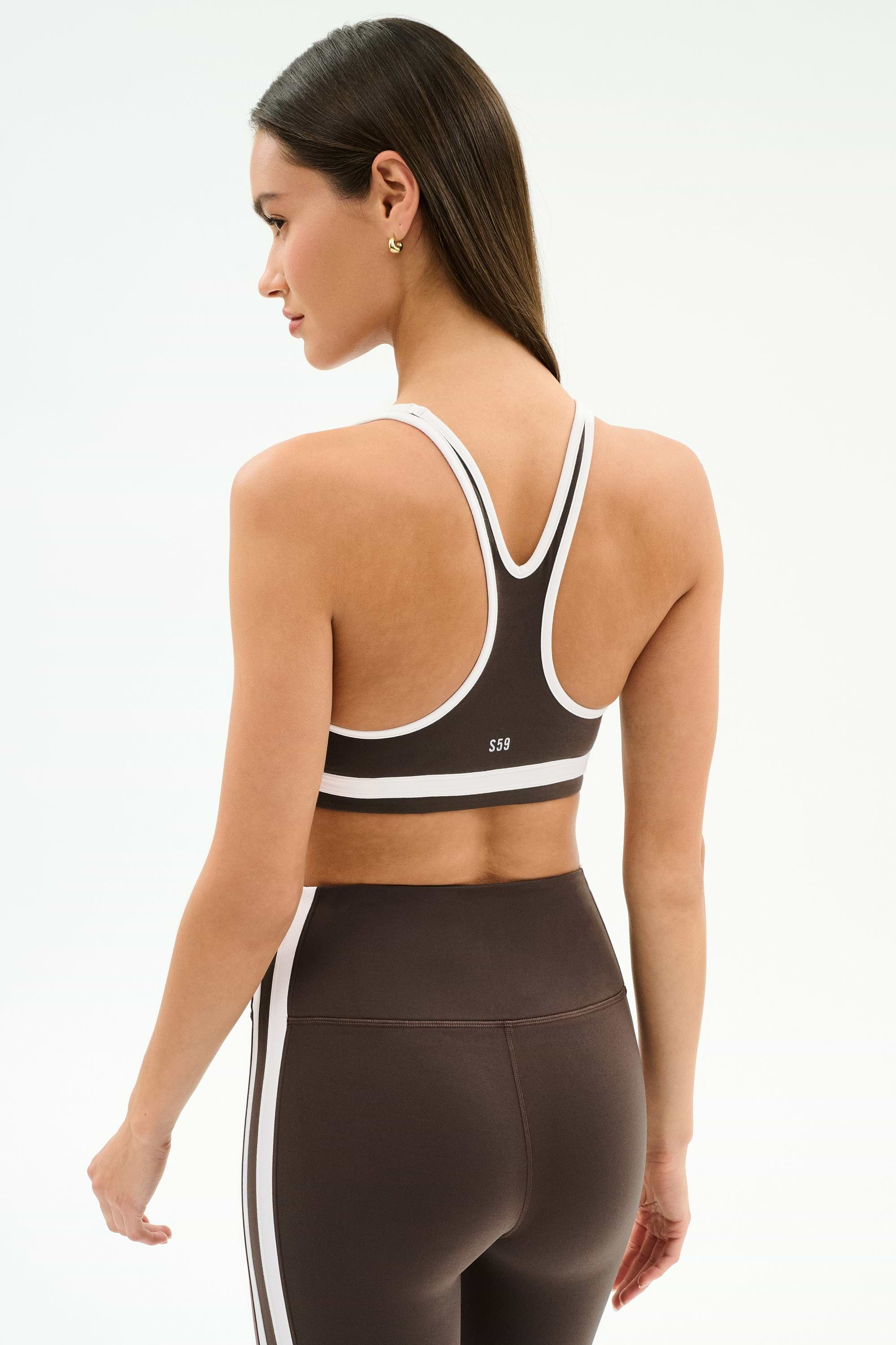 A woman models the SPLITS59 Bianca Rigor Bra in Dark Chocolate/White, paired with matching high-waisted leggings, seen from the back against a light backdrop—perfect for high-impact workouts or intense gym sessions.