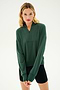 A woman with blonde hair wears the Birdie Fleece Half Zip - Military from SPLITS59 and black shorts, standing with her hands clasped in front of a plain light background.