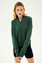 A woman with blonde hair wears the Birdie Fleece Half Zip - Military from SPLITS59 and black shorts, standing with her hands clasped in front of a plain light background.