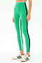 A person wearing SPLITS59 Sam High Waist Rigor 7/8 leggings in Spearmint/Indigo, featuring a black side stripe and paired with white sneakers with green stripes, stands against a plain light background.