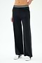 A person wears the SPLITS59 Michele Airweight Trouser in black, featuring a wide-leg cut and a white and black striped waistband, paired with white sneakers, standing against a plain light background.