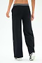 Someone stands facing away, wearing SPLITS59 Michele Airweight Trouser in black with a white-striped waistband and white sneakers against a plain backdrop.