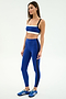 Woman wears the SPLITS59 Clare High Waist Rigor 7/8 in Cobalt/Black, paired with blue Adidas sneakers—crafted from durable Rigor fabric and ideal for gym workouts—posing against a plain white background.