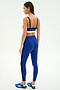 A woman faces away, wearing SPLITS59’s Clare High Waist Rigor 7/8 leggings in Cobalt/Black rigor fabric and a blue sports bra, styled with blue Adidas sneakers—designed for intense gym workouts.