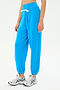 A person wears SPLITS59's Andie Oversized Fleece Sweatpant in Riviera, bright blue with a white drawstring, paired with white athletic sneakers, and stands against a plain light background.