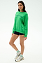 A woman stands against a white background wearing the SPLITS59 Andie Oversized Fleece Varsity Graphic Sweatshirt in Grass, black shorts, white socks, and white sneakers.