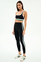 Woman wearing the SPLITS59 Bianca Rigor Bra in Black/White, paired with high-waisted leggings with white and green stripes and white Adidas sneakers, standing against a plain white background.