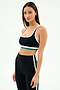 A woman wears the SPLITS59 Bianca Rigor Bra in Black/White with matching high-waisted black leggings featuring white and green stripes, standing against a plain light background.