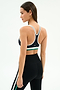 A woman stands in profile wearing the SPLITS59 Bianca Rigor Bra - Black/White, a black spandex sports bra with white and green trim, paired with black nylon leggings featuring a white and green side stripe.