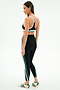 A woman stands sideways wearing the SPLITS59 Bianca High Waist Rigor 7/8 leggings in Black/White, featuring white and green stripes, paired with a black sports bra and white athletic shoes with green stripes.