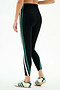 A person wears the SPLITS59 Bianca High Waist Rigor 7/8 leggings in Black/White—stretch fabric with green and white side stripes—paired with white sneakers featuring green stripes, standing against a plain white background.