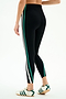 A person wears the SPLITS59 Bianca High Waist Rigor 7/8 leggings in Black/White—stretch fabric with green and white side stripes—paired with white sneakers featuring green stripes, standing against a plain white background.