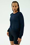 A woman with braided hair models the SPLITS59 Brooks Fleece Long Sleeve Sweatshirt in indigo and black biking shorts against a plain white background. Made in Los Angeles.