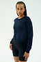 A woman with braided hair models the SPLITS59 Brooks Fleece Long Sleeve Sweatshirt in indigo and black biking shorts against a plain white background. Made in Los Angeles.