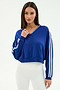 A woman models the SPLITS59 Ellie Fleece V Neck Sweatshirt in Cobalt/White, featuring white sleeve stripes, paired with white ribbed leggings against a plain background for an athletic look.