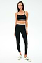 A woman stands facing forward, wearing the SPLITS59 Sam High Waist Rigor 7/8 leggings in Black/Military and a matching sports bra with white stripes, paired with white sneakers featuring green accents.