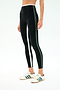 A person wears SPLITS59 Sam High Waist Rigor 7/8 leggings in Black/Military, featuring white and green side stripes, paired with white Adidas sneakers with green stripes, standing against a plain background.