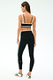 A woman faces away from the camera in SPLITS59's Sam High Waist Rigor 7/8 leggings and matching black sports bra with green stripes, paired with white sneakers accented in green.