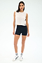 A woman stands against a white background wearing the SPLITS59 Logan Mesh Tank With Stripe in White/Indigo, black fitted shorts, white socks, and white sneakers—an ideal look for breathable sportswear.