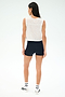 A woman faces away, wearing the SPLITS59 Logan Mesh Tank With Stripe in White/Indigo as a sleeveless workout top, paired with black shorts, white socks with black stripes, and white athletic shoes against a plain light background.