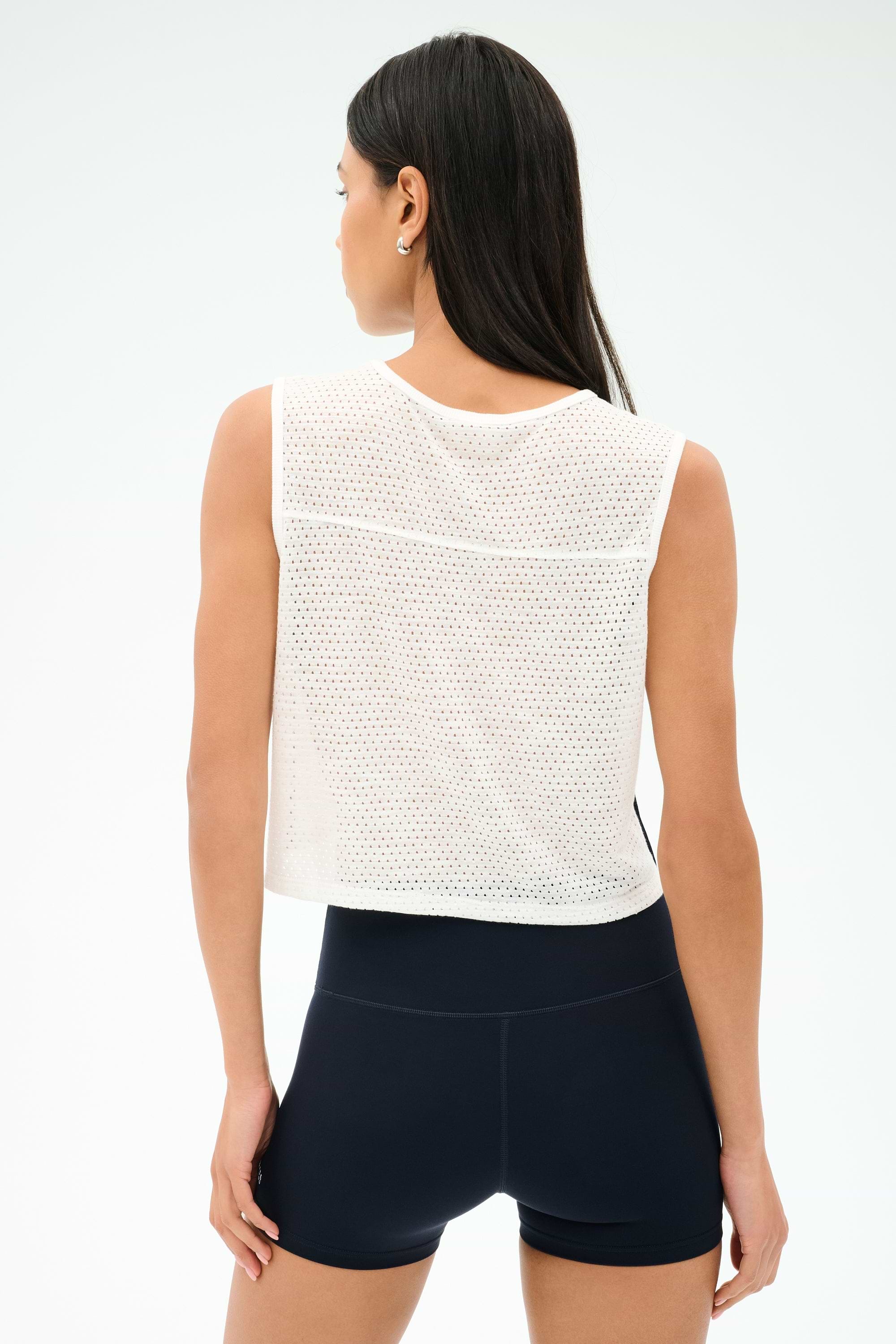 A woman stands with her back to the camera, wearing SPLITS59's Logan Mesh Tank With Stripe in White/Indigo and black athletic shorts—perfect breathable sportswear against a plain background.