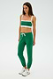 A person in green SPLITS59 Sonja Fleece Sweatpant in Arugula, a green and white sports bra, and white sneakers stands on a plain background.