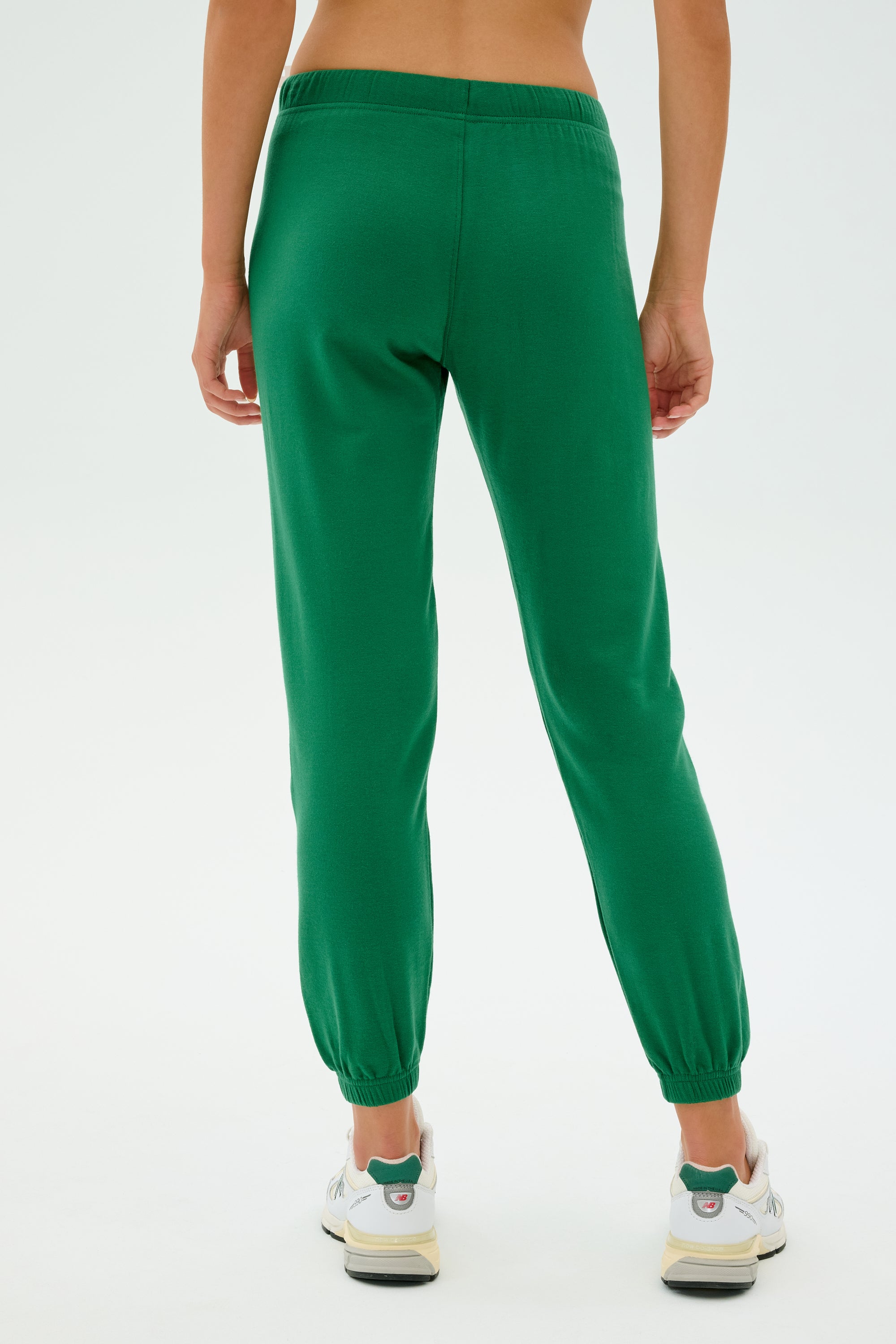 A person wearing SPLITS59's Sonja Fleece Sweatpant in Arugula and white sneakers stands on a plain background.