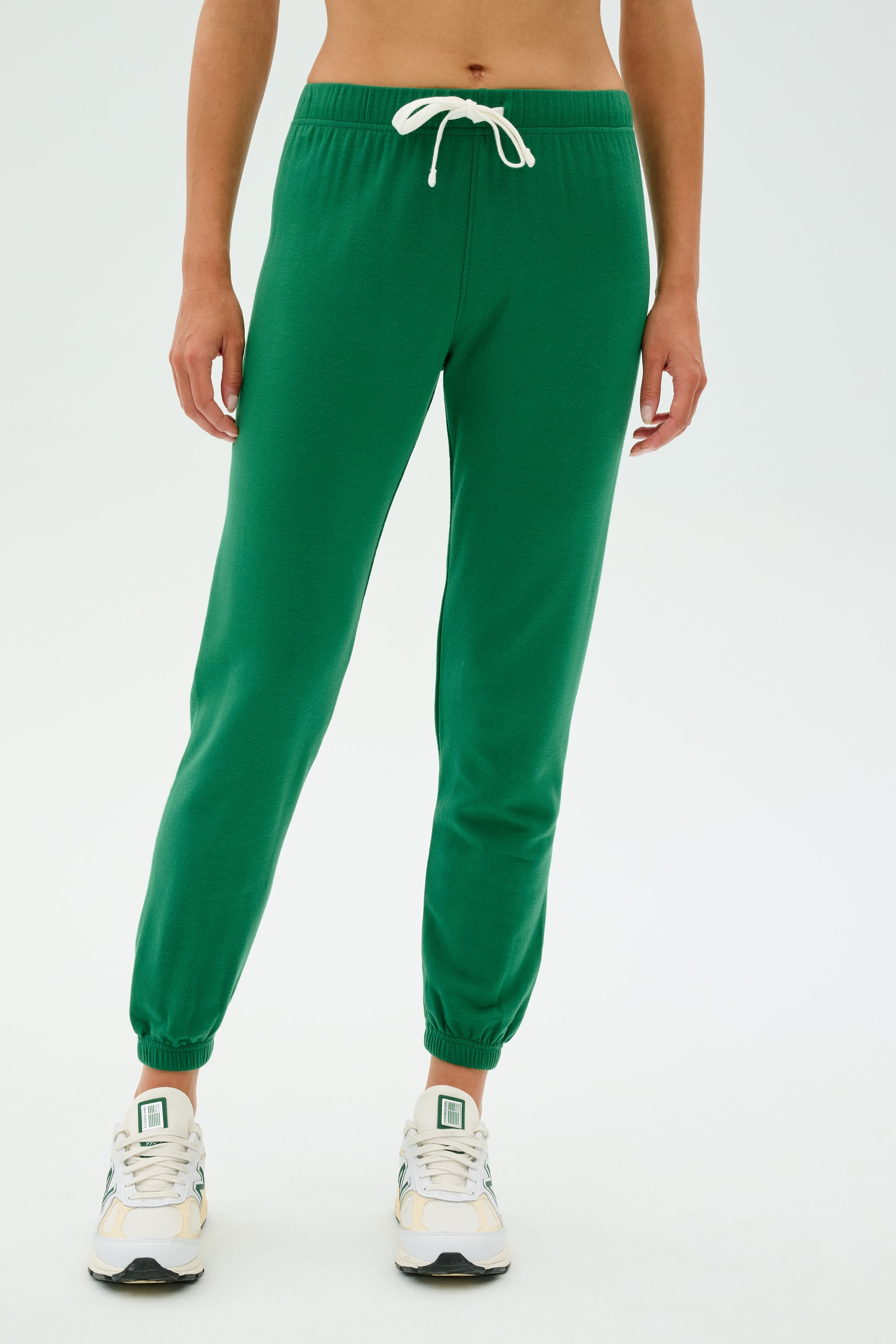 Someone wearing the Sonja Fleece Sweatpant in Arugula from SPLITS59 and white sneakers stands against a plain background.