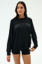A woman wears the SPLITS59 Andie Oversized Fleece Varsity Graphic Sweatshirt in black with "LOS ANGELES" text, paired with matching black shorts, standing against a plain light background.