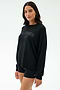 A woman wears the SPLITS59 Andie Oversized Fleece Varsity Graphic Sweatshirt in Black/Splits59 Los Angeles and black shorts, made in Los Angeles, standing against a plain light background.