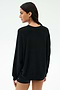 A woman stands against a light background, facing away and looking over her shoulder, wearing the SPLITS59 Andie Oversized Fleece Varsity Graphic Sweatshirt in black by Splits59 Los Angeles.
