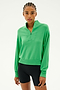 A person dressed in the SPLITS59 Birdie Fleece Half Zip in Grass and black shorts stands against a simple background, prepared for winter workouts.