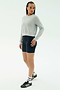 A person stands slightly to the side wearing the SPLITS59 Brooks Fleece Long Sleeve Sweatshirt in Heather Grey, paired with navy cycling shorts, white socks, and black Adidas sneakers against a plain light background.