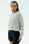 A person with braided hair wears the SPLITS59 Brooks Fleece Long Sleeve Sweatshirt in Heather Grey and black fitted spandex-blend shorts, standing against a plain light background.