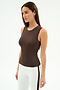 A woman stands against a white background wearing the SPLITS59 Carter Airweight Lite Tank in Dark Chocolate, paired with white pants featuring a dark side stripe.