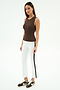 A woman stands against a white background wearing the SPLITS59 Carter Airweight Lite Tank in Dark Chocolate, paired with white pants featuring a black side stripe and brown sneakers.