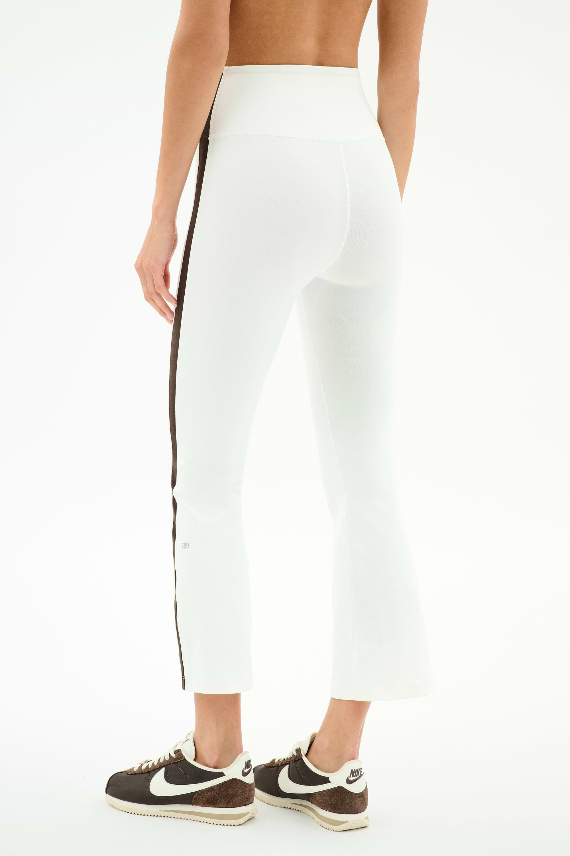 A person is shown from the back wearing SPLITS59 Raquel High Waist Supplex Crop in White/Dark Chocolate, featuring a high-waisted fit and dark chocolate side stripe, paired with black Nike sneakers against a plain background.