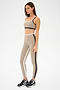 Wearing SPLITS59's Sam High Waist Rigor 7/8 in Latte/Black, one stands poised in a beige athletic ensemble with black accents, exuding workout energy. Black sneakers complete the look as they face slightly right against a simple backdrop.