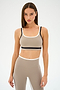 A model in a beige and black athletic outfit showcases the SPLITS59 Eva Rigor Double Strap Bra in Latte/Black against a plain backdrop.