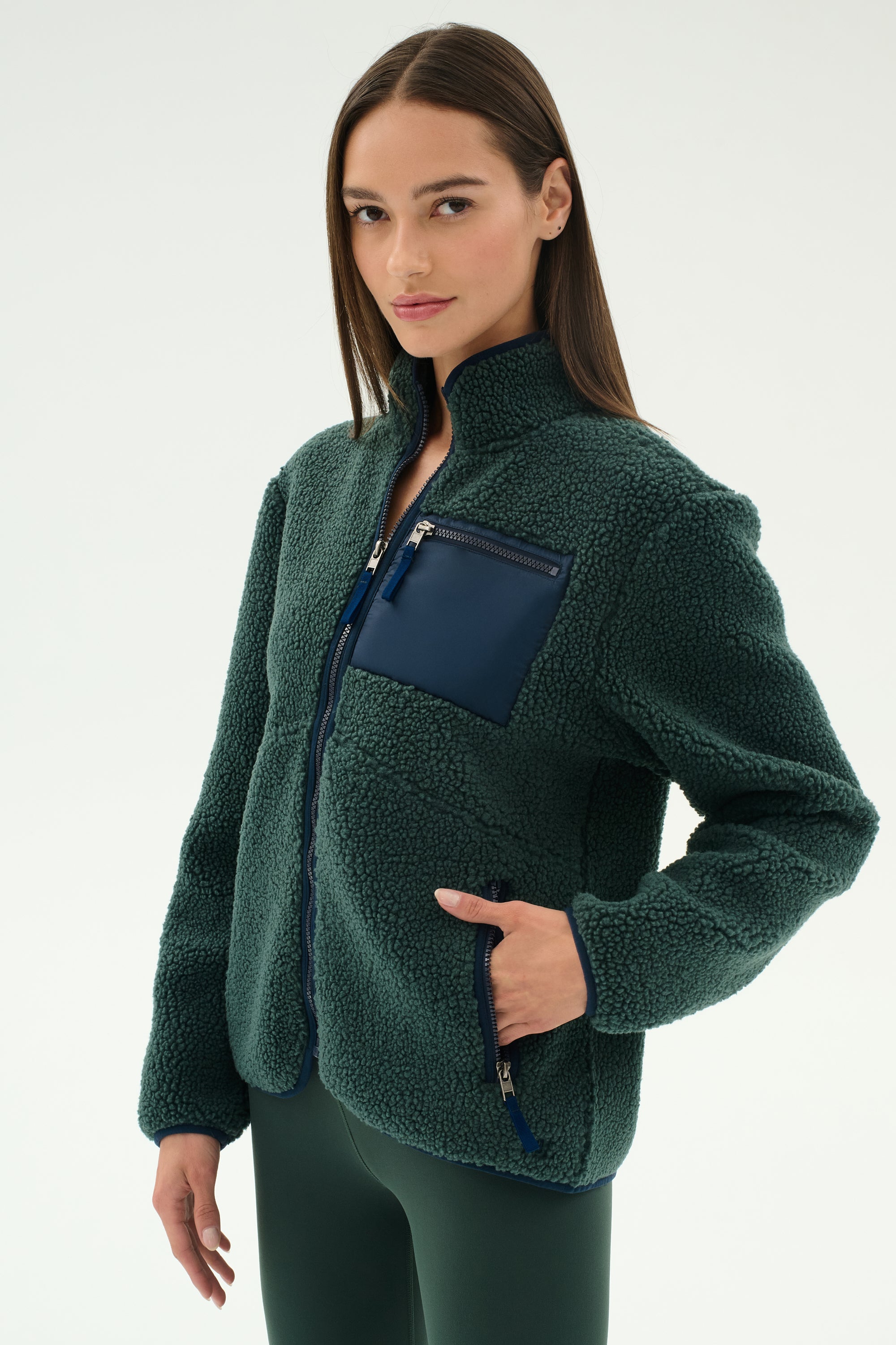 A woman wears the SPLITS59 Harris Sherpa Jacket in Military/Indigo, featuring a zippered navy chest pocket, along with matching pants, standing against a plain light background.