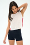 A woman in the SPLITS59 Logan Mesh Tank With Stripe - White/Pirate Red stands with one hand on her neck, gazing downward, paired with black shorts.