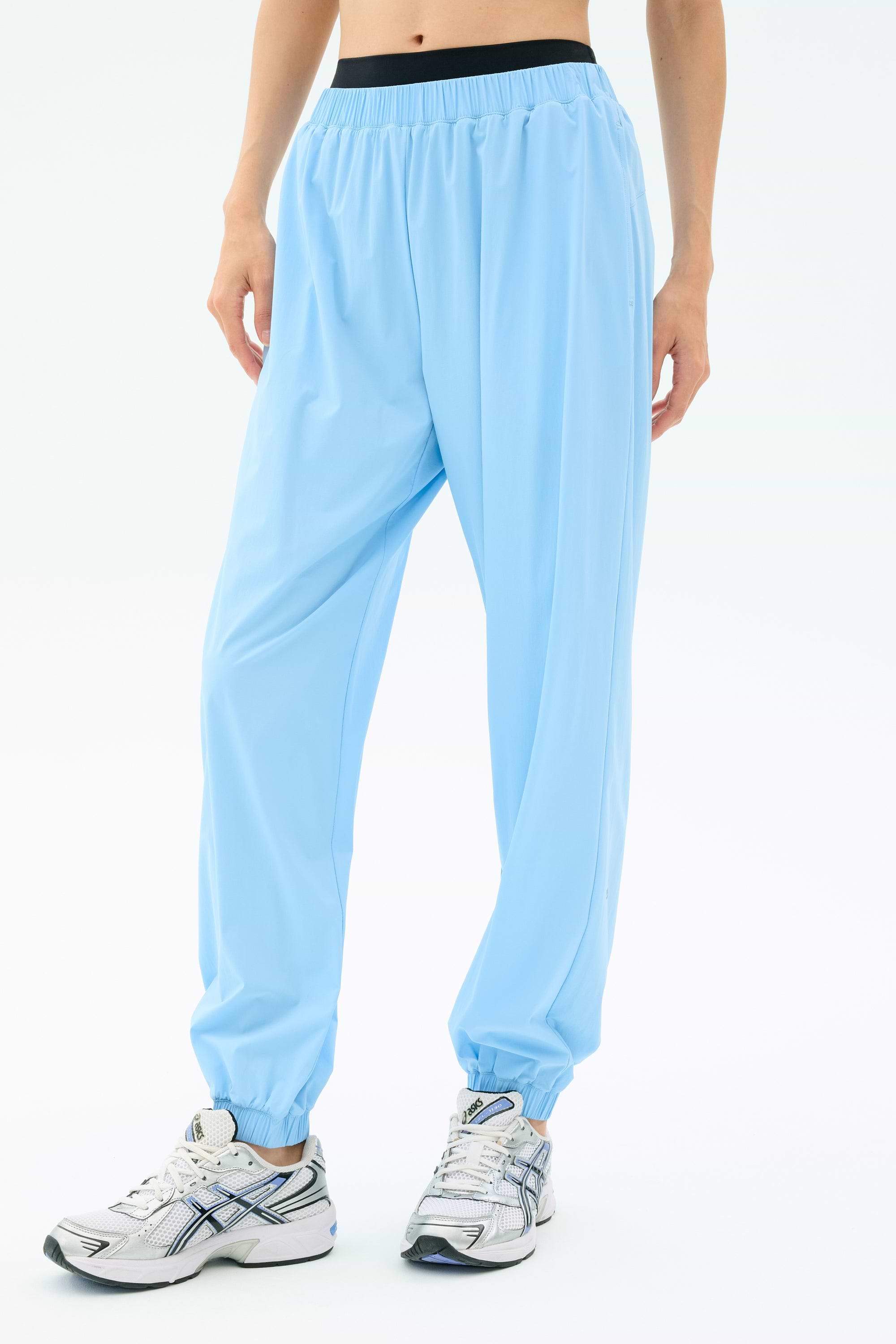 A person wears SPLITS59 Megan Woven Nylon Jogger in Skylight with white athletic shoes, standing against a plain light background. Only the lower body is visible.