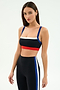 A woman models the SPLITS59 Monah Rigor Bra in Black/Cobalt, paired with black high-waisted leggings featuring blue and white side stripes, posed against a plain light background.