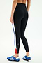 A person is wearing SPLITS59 Monah High Waist Rigor Legging 7/8 in Black/Cobalt, featuring blue, white, and red side stripes, paired with blue athletic shoes, standing against a plain background.