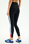 A person is wearing SPLITS59 Monah High Waist Rigor Legging 7/8 in Black/Cobalt, featuring blue, white, and red side stripes, paired with blue athletic shoes, standing against a plain background.