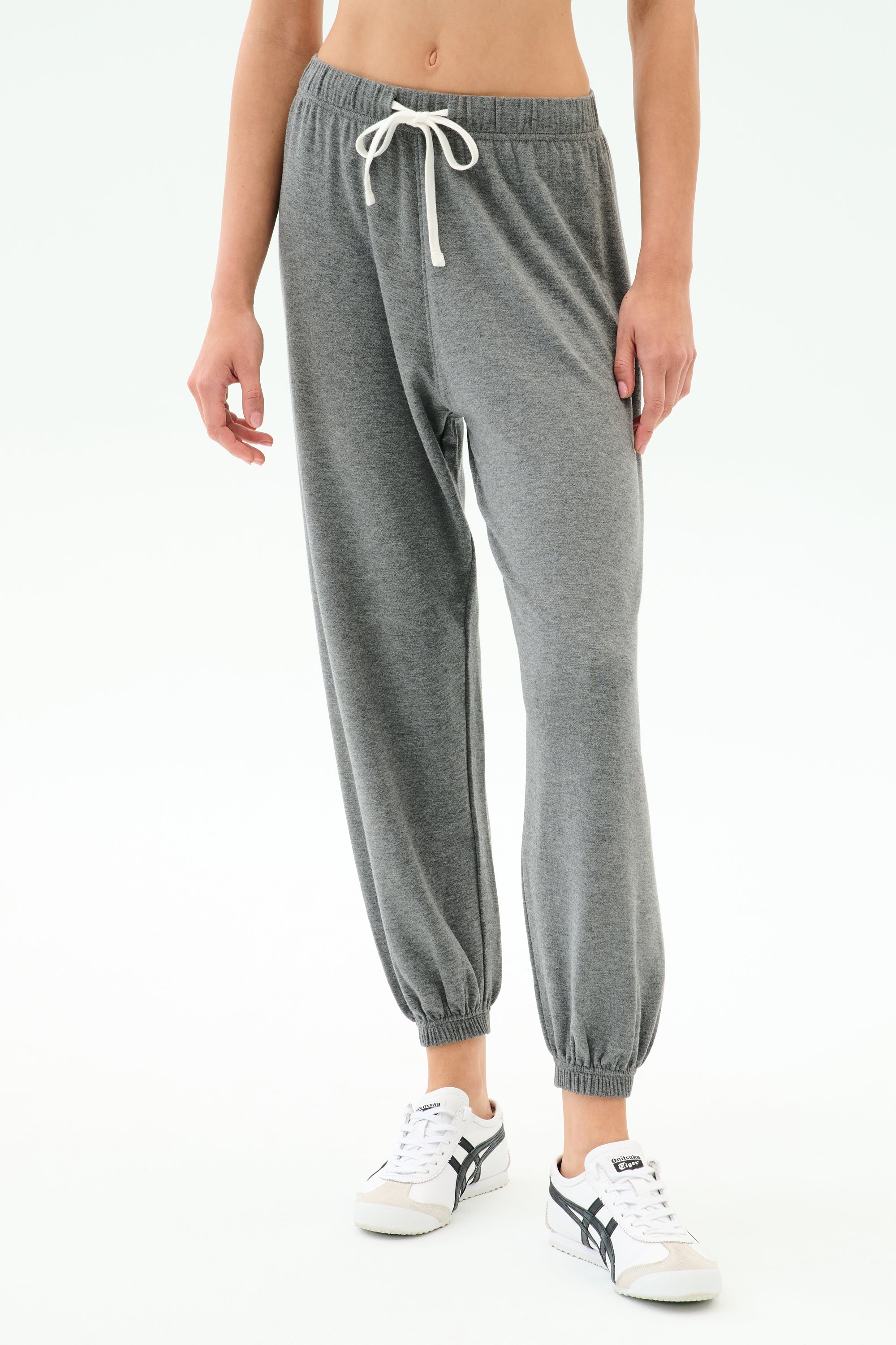 A person wearing SPLITS59 Andie Oversized Fleece Sweatpant in Medium Heather Grey and white sneakers, shown from midriff to feet against a plain background—made in Los Angeles and perfect for cool weather workouts.