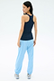 A woman stands facing away, wearing the SPLITS59 Ashby Rib Tank in Indigo, light blue joggers, and white sneakers against a plain white background.
